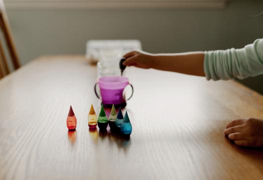 Child's arm reaching out to add drops of food coloring to a cup of water | Merry Maids