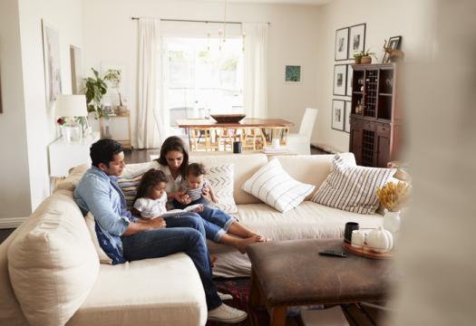 Family of four reading a book on the couch in a clean and tidy living room. | Merry Maids®
