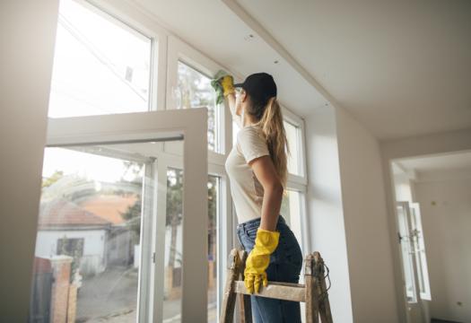 Woman on ladder in yellow gloves cleaning window with rag | Merry Maids